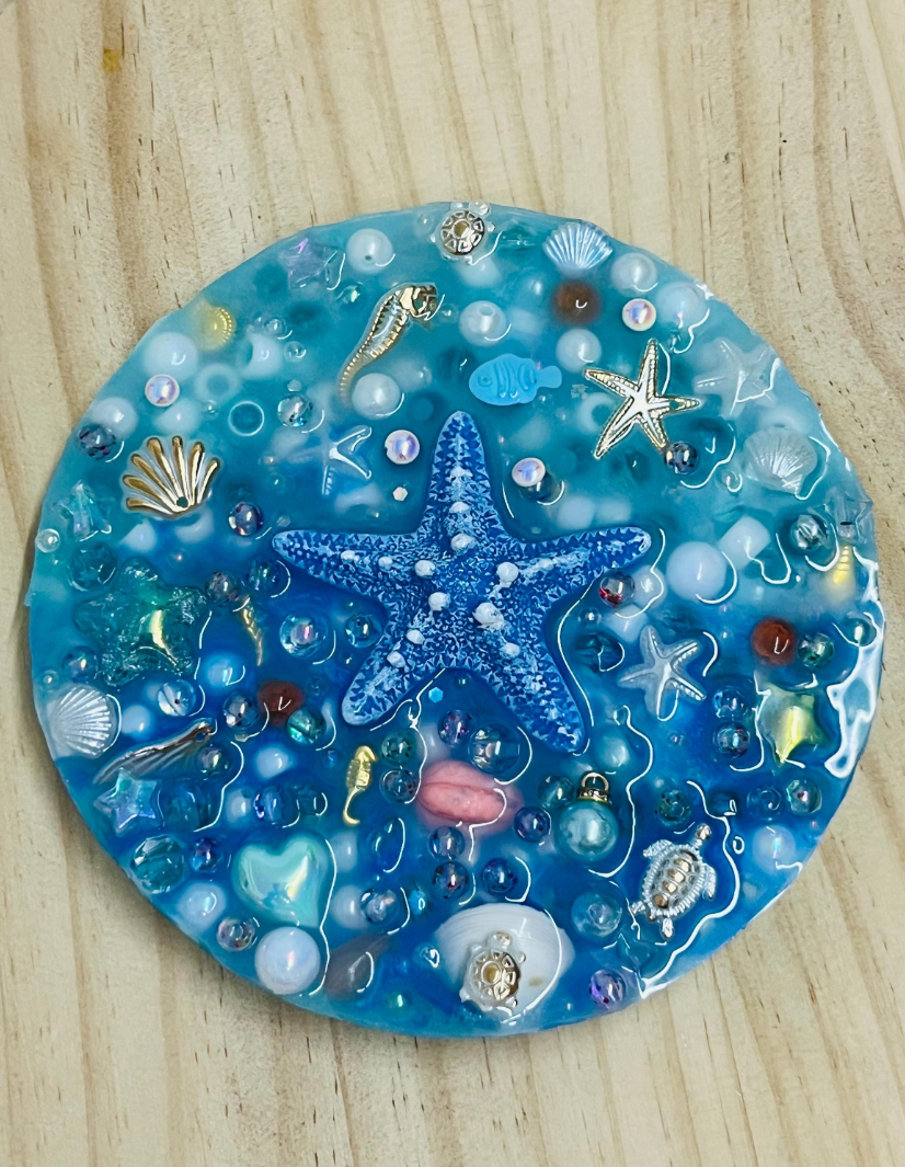 Decorative coaster with starfish, shells, and bubbles on a wooden surface